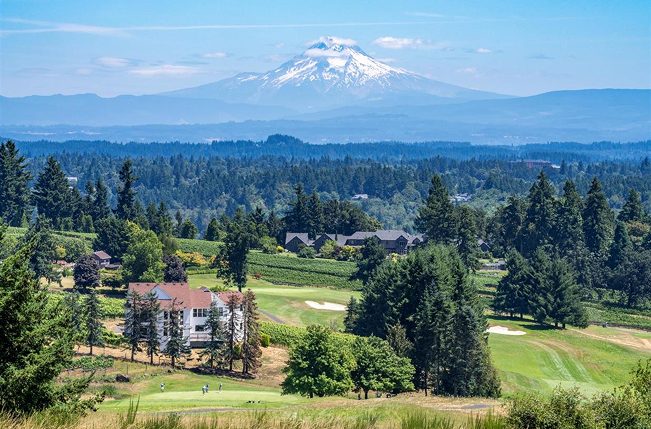 Fairway and clubhouse surrounded by evergreens with snow-capped Mount Hood in the distance at The Oregon Golf Club in West Linn, Oregon