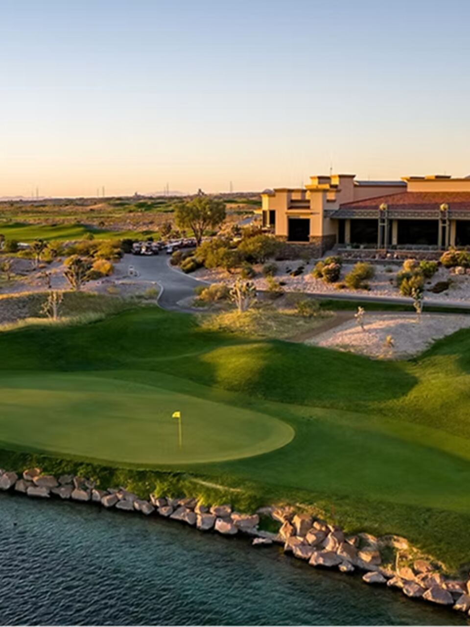 Desert green beside a rock-lined water hazard at sunset with the clubhouse behind at Paiute Golf Course in Las Vegas, Nevada