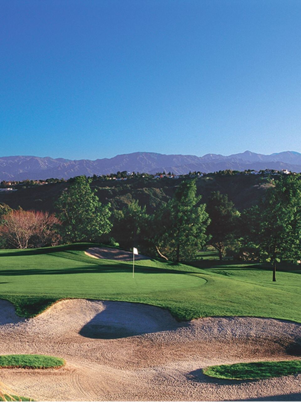 Bunkered green framed by trees with the San Gabriel Mountains beyond at MountainGate Country Club in Los Angeles, California